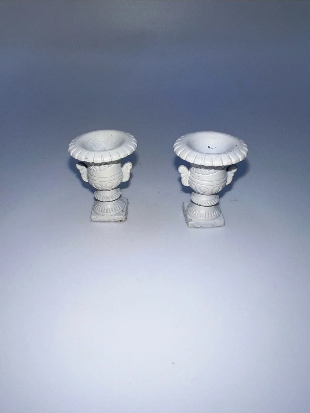 Miniature Medici-style vases feature a classic white finish and ornate pedestal